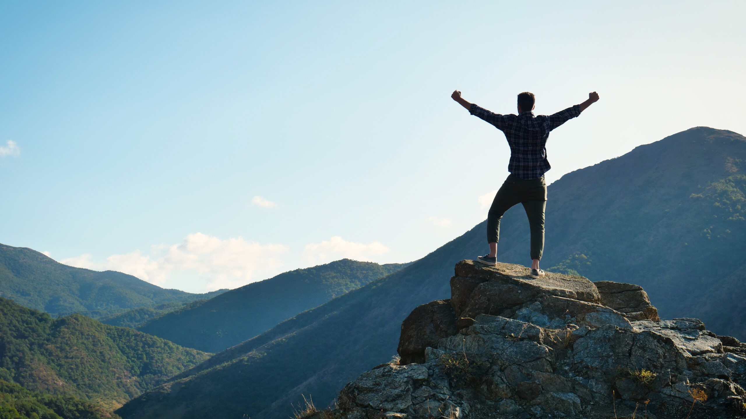 A person stands triumphantly on a rocky outcrop, arms raised
